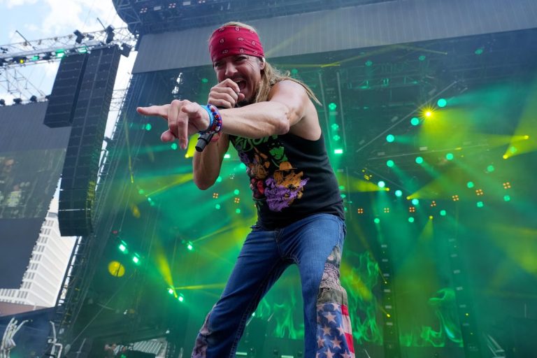 Bret Michaels of Poison performing onstage in a red bandana and sleeveless shirt, pointing at the crowd under green stage lights