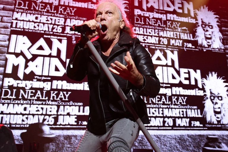 Iron Maiden and Christopher Cross Take Aim at Trump’s ‘Lake America’ From Toronto Stages Iron Maiden singer Bruce Dickinson sings into a handheld microphone on stage in a black leather jacket, in front of a large screen showing vintage black-and-white Iron Maiden concert posters