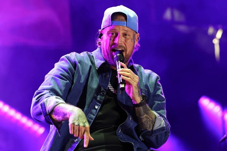 Jelly Roll performing onstage in a denim jacket and backwards cap, pointing toward the audience