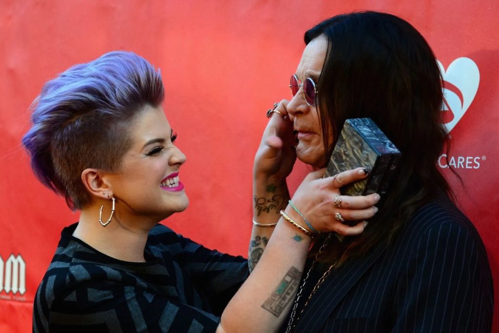 Kelly Osbourne: Ozzy Came Straight Home After He Died, Not to a Morgue Kelly Osbourne laughing as she holds her father Ozzy Osbourne's face at a red-carpet event