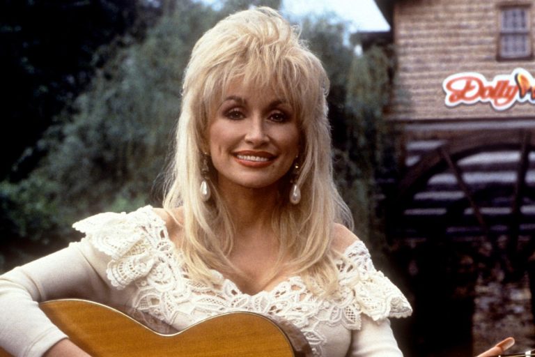 Dolly Parton smiling and holding an acoustic guitar outdoors at Dollywood in 1993