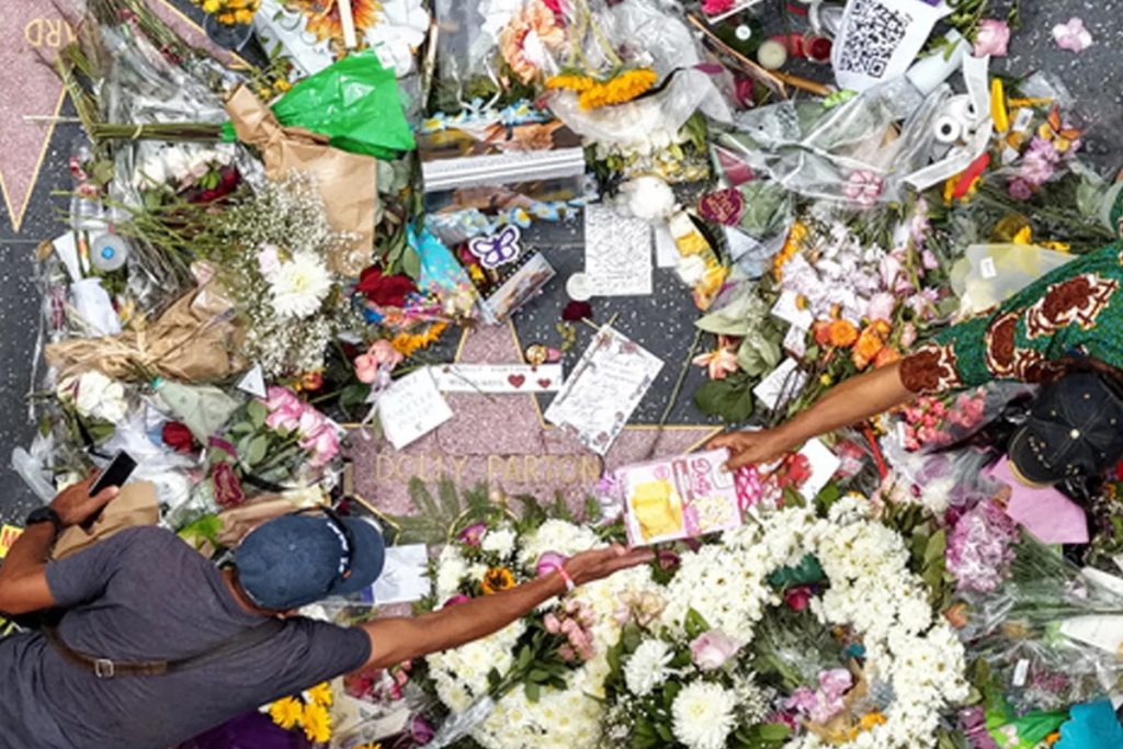 Overhead view of Dolly Parton's Hollywood Walk of Fame star covered in flowers, candles and handwritten cards, with two mourners reaching in to place tributes