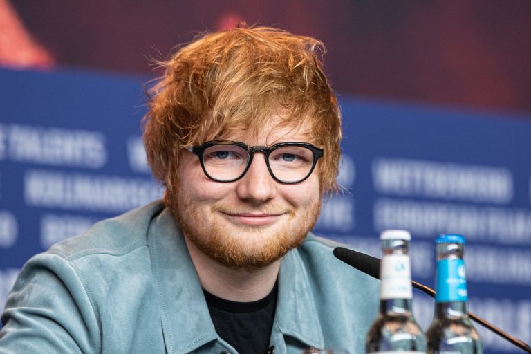 Ed Sheeran’s Gillette Stadium Shows Canceled as Macklemore Row Hangs Over Robert Kraft’s Venue Ed Sheeran smiling at a press conference table with microphones and water bottles
