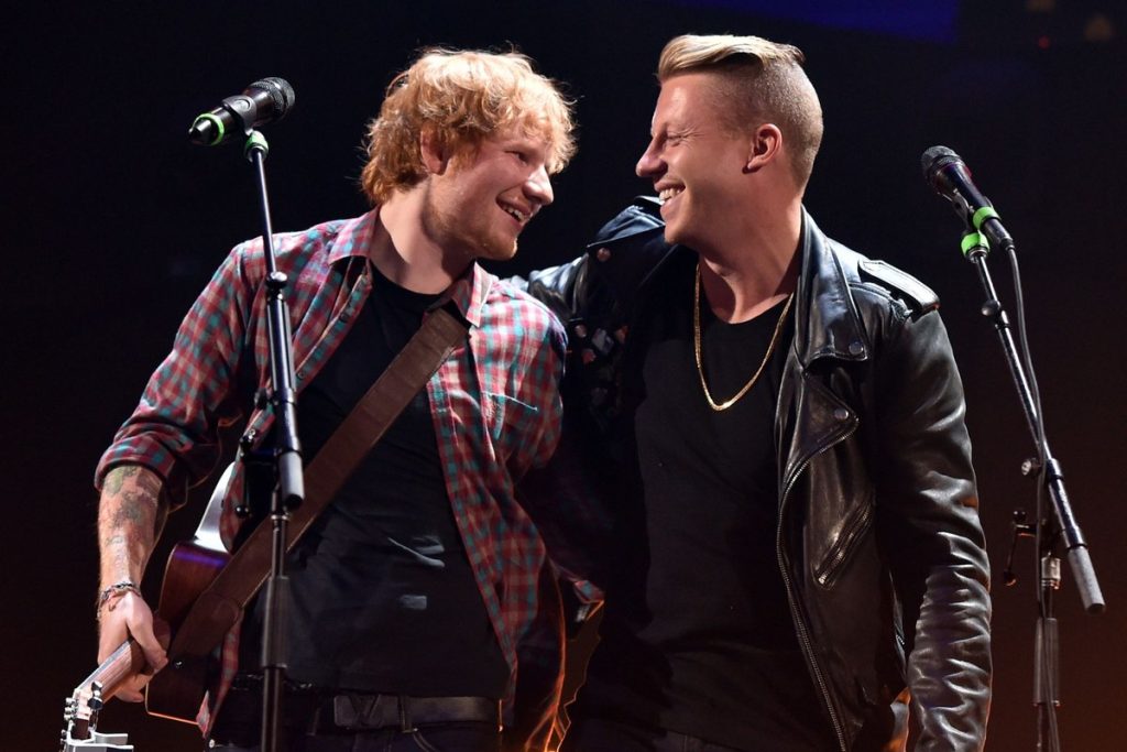 Ed Sheeran Breaks His Silence on Macklemore’s Tour Removal: “I Am Not Complicit” Ed Sheeran and Macklemore laughing together on stage, Sheeran holding an acoustic guitar