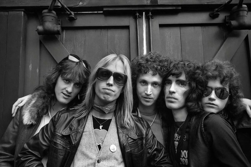Tom Petty’s Original Heartbreakers Reunite at the Ryman, With Chris Stapleton Singing in His Place Black and white 1970s portrait of the five original members of Tom Petty and the Heartbreakers standing together against a wooden door, Tom Petty in sunglasses at the center