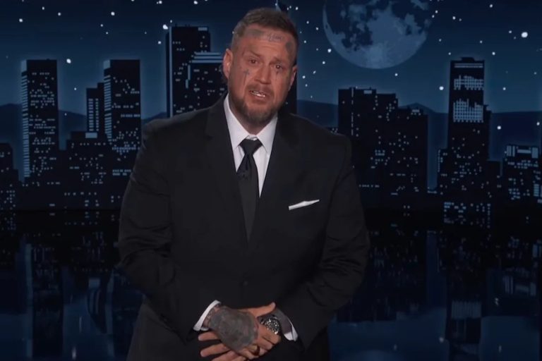 Jelly Roll Dropped From Mar-a-Lago Police Fundraiser Over Jimmy Kimmel Trump Jokes Jelly Roll in a black suit and tie standing behind the desk on Jimmy Kimmel Live, with the show's illuminated night-time city skyline backdrop behind him