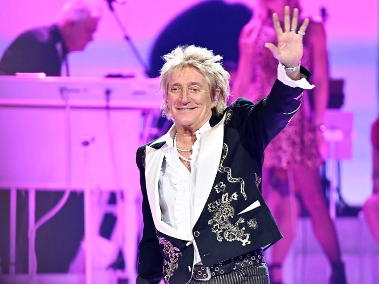 Rod Stewart Announces The Final Encore: ‘Most Definitely My Last’ Tour After a Year of Health Scares Rod Stewart smiling and waving to the crowd on stage in an embroidered black jacket