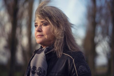 Suzi Quatro on Her Rock Hall Snub: ‘I Just Hope They’re Not Waiting for Me to Die’ Suzi Quatro in a black leather jacket and skull-print scarf, looking off to one side, photographed outdoors among bare trees