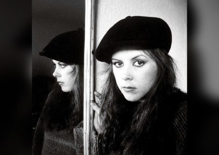 Kirsty MacColl in a black beret photographed beside her mirror reflection