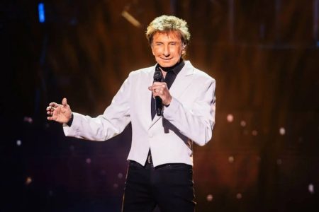 Barry Manilow in a white jacket singing into a microphone on stage at the Westgate Las Vegas