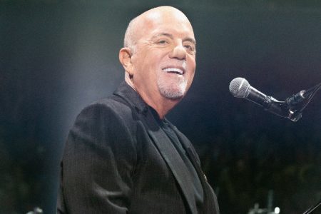 Billy Joel Says He Isn’t Allowed to Drive as Doctors Weigh Whether He Can Perform Again Billy Joel smiling at the piano microphone on stage in a dark jacket