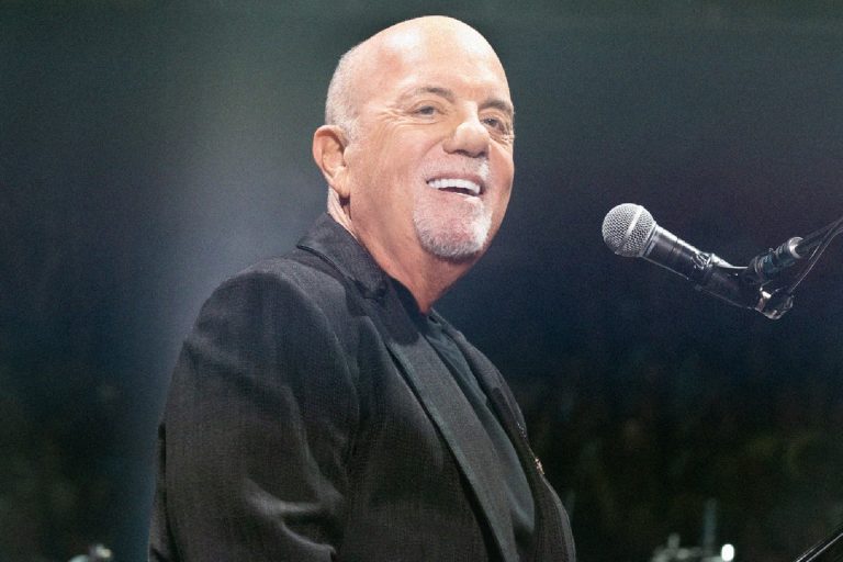 Billy Joel Says He Isn’t Allowed to Drive as Doctors Weigh Whether He Can Perform Again Billy Joel smiling at the piano microphone on stage in a dark jacket