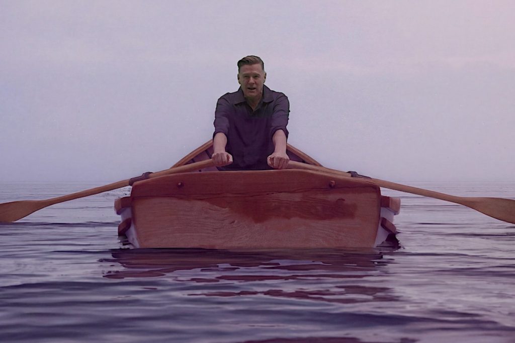 Bryan Adams Answers Trump’s ‘Lake America’ Order With New Song ‘Lake Ontario’ Bryan Adams rowing a wooden boat across calm water in the Lake Ontario music video