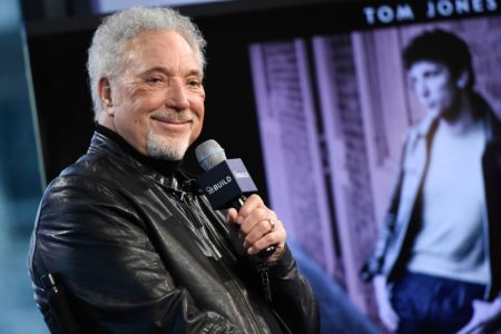 Tom Jones in a black leather jacket smiling while holding a microphone at a Q&A event