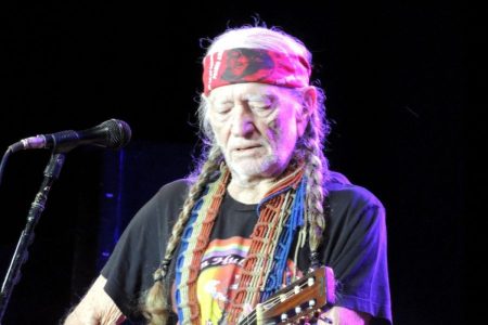 Willie Nelson in a red bandana playing guitar onstage